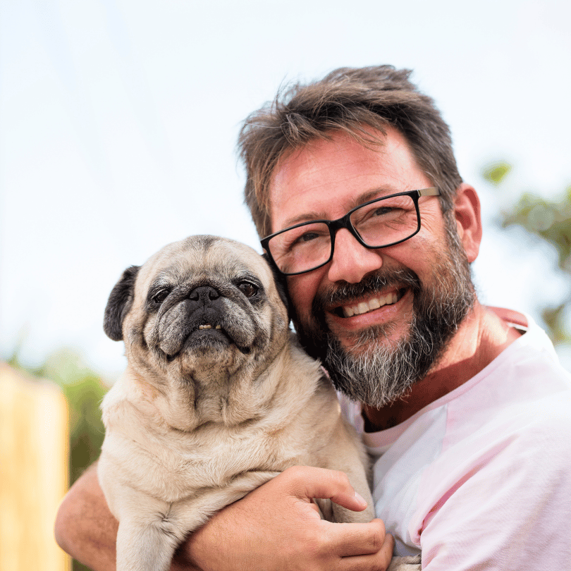 A man wearing glasses smiles warmly while holding his pug outside, embodying the essence of Home and loyalty.