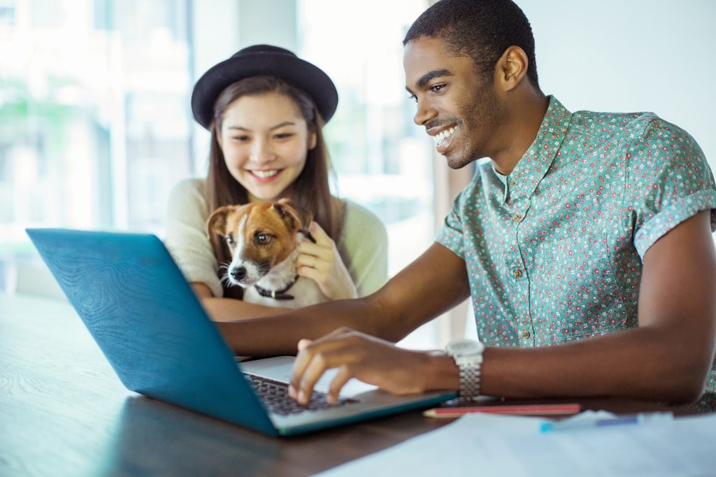 Young couple with their dog using RunLoyal pet care software on a laptop.
