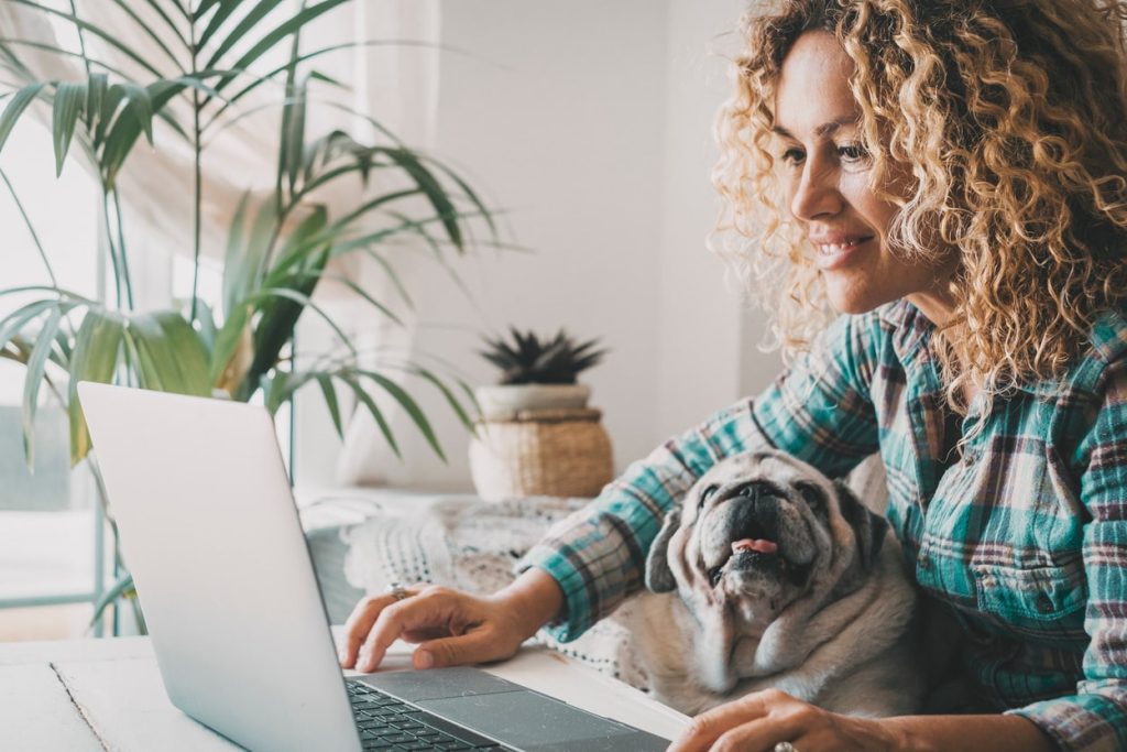 Woman with curly hair using laptop next to her bulldog at home, browsing RunLoyal.